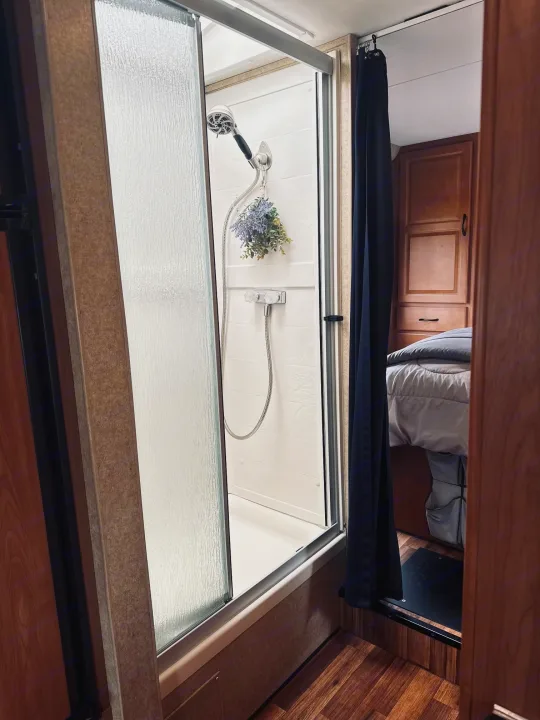 Inside an RV rental: a modern shower with textured glass, beside a dark privacy curtain leading to the bedroom.. Thor Majestic 2016