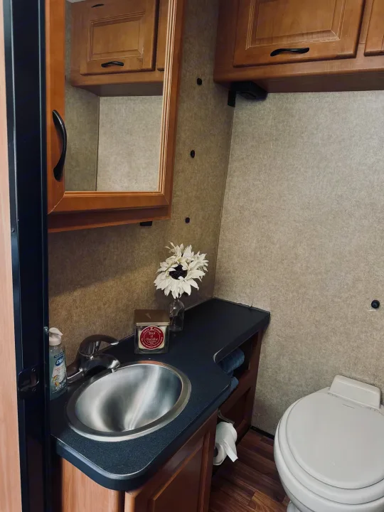 Functional RV rental bathroom interior with a stainless steel sink, dark counter, wood cabinets, and toilet.. Thor Majestic 2016