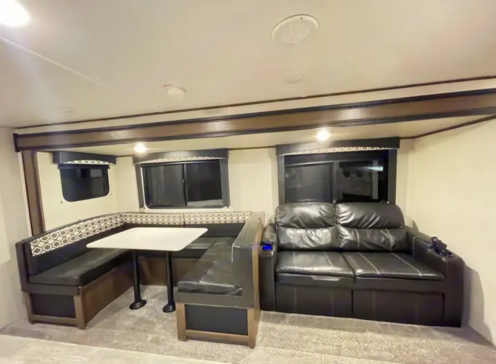 Inside an RV rental: cozy living area featuring a U-shaped dinette with table and a comfortable black leather sofa.. Forest River PRIME TIME AVENGER 2021