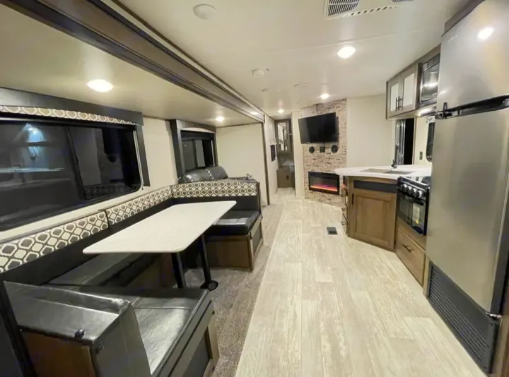 Spacious RV rental interior: kitchen with fridge/oven, dining booth, and living area with fireplace/TV. Modern design for travel comfort.. Forest River PRIME TIME AVENGER 2021
