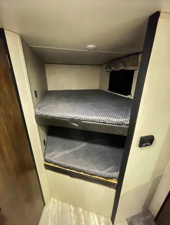 Compact RV rental interior featuring two comfortable bunk beds with patterned sheets and a window, ideal for travel.. Forest River PRIME TIME AVENGER 2021