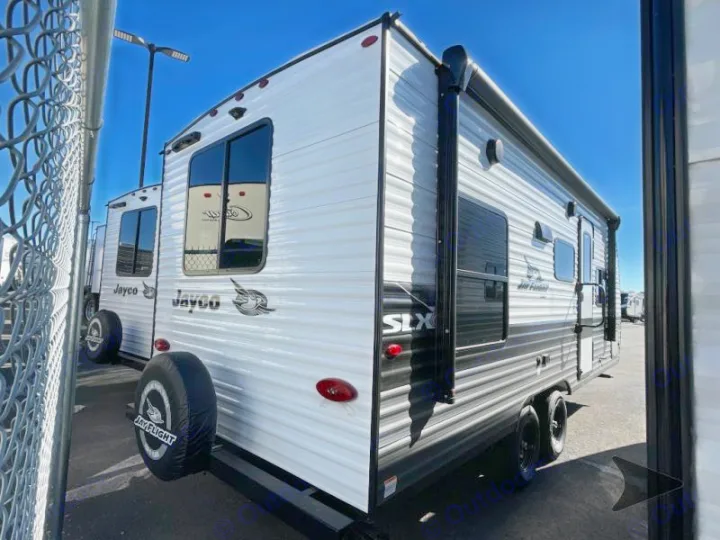 White Jayco travel trailer with black trim, awning, and spare tire in a sunny lot, available for rv rental.. Jayco Jay Flight 2024