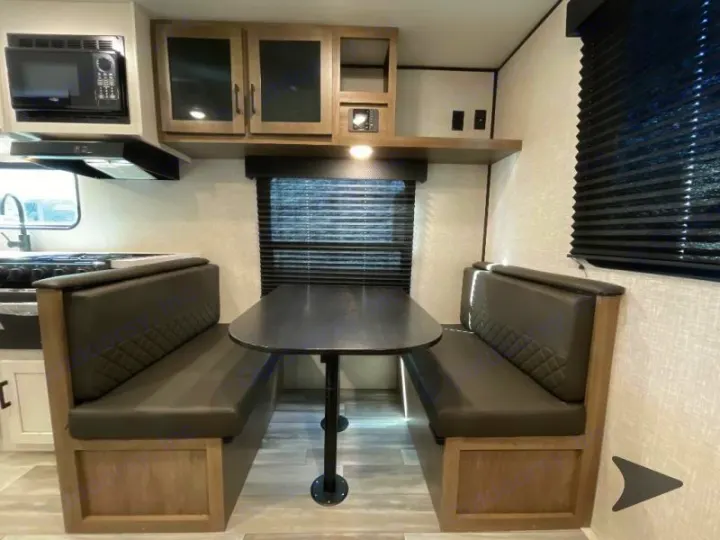 Compact RV rental interior featuring a dinette with booth seating, table, and a partial kitchen. Ideal for road trips.. Jayco Jay Flight 2024