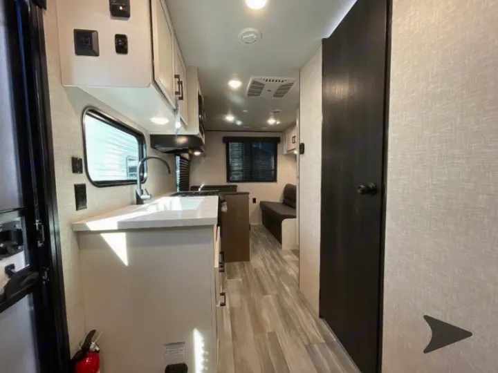 Inside a modern RV rental: a bright kitchen with white counters, sink, and cabinets, opening to a living area. Perfect for trips.. Jayco Jay Flight 2024