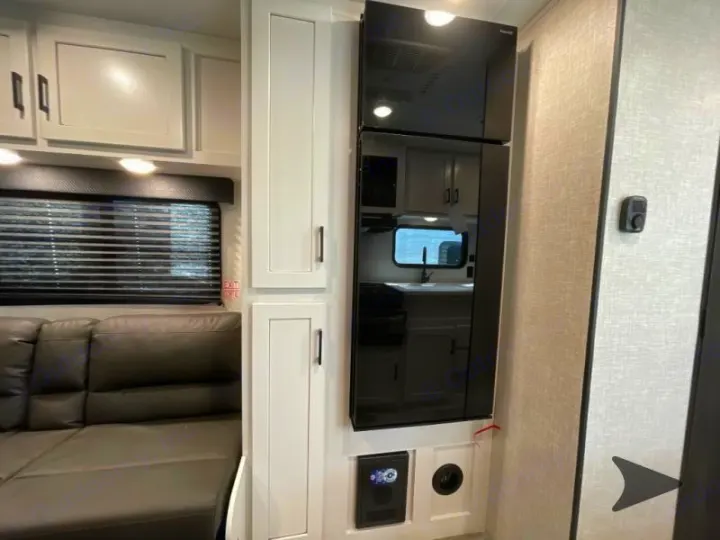 Modern RV rental interior, showing a sleek black refrigerator, white cabinets, and a gray sofa by a window.. Jayco Jay Flight 2024