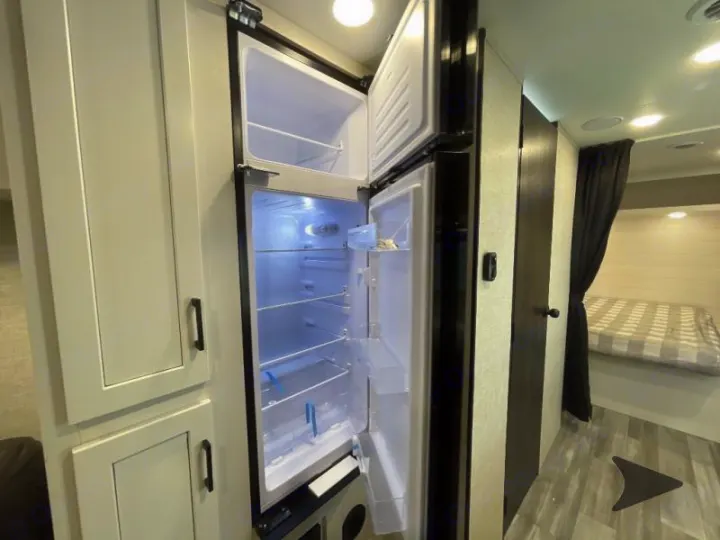 Explore this RV rental's interior: an open fridge, light cabinets, and a cozy bedroom beyond the privacy curtain.. Jayco Jay Flight 2024