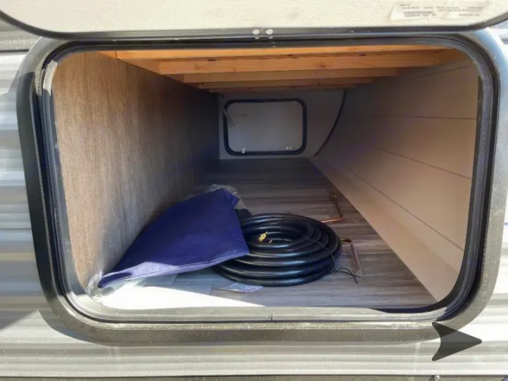 Spacious RV rental exterior storage bay with coiled hose, blue bag, and rear access panel for camping essentials.. Jayco Jay Flight 2024