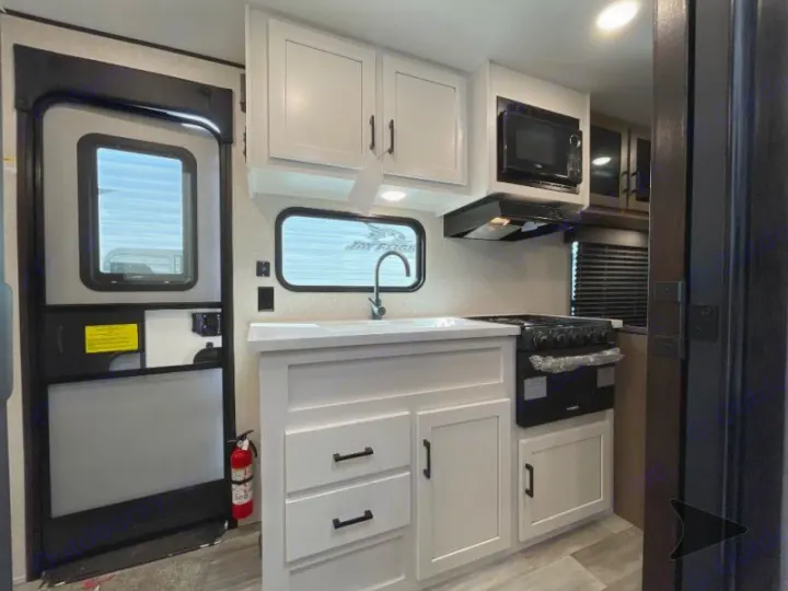 Step into a modern RV rental featuring a white-cabinet kitchen with microwave, stove, sink, and an entrance door.. Jayco Jay Flight 2024