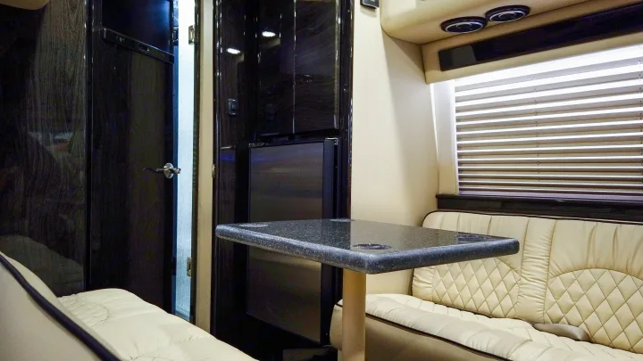 Luxury RV rental interior with cream leather benches, a dark speckled table, and sleek wood cabinetry, perfect for travel.. Ultimate Toys Ultimate RV 2024