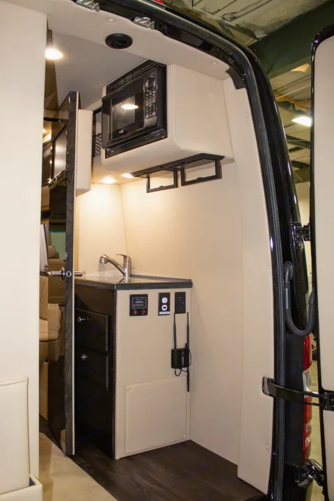 Inside an RV rental, a sleek kitchenette with microwave, sink, and control panel, designed for comfort and convenience on the road.. Ultimate Toys Ultimate RV 2024