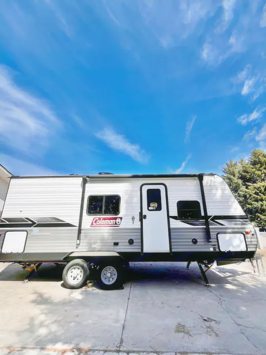A Coleman travel trailer, ideal for rv rental, is seen parked on a driveway beneath a blue sky with wispy clouds.. Dutchmen Coleman Lantern 2023