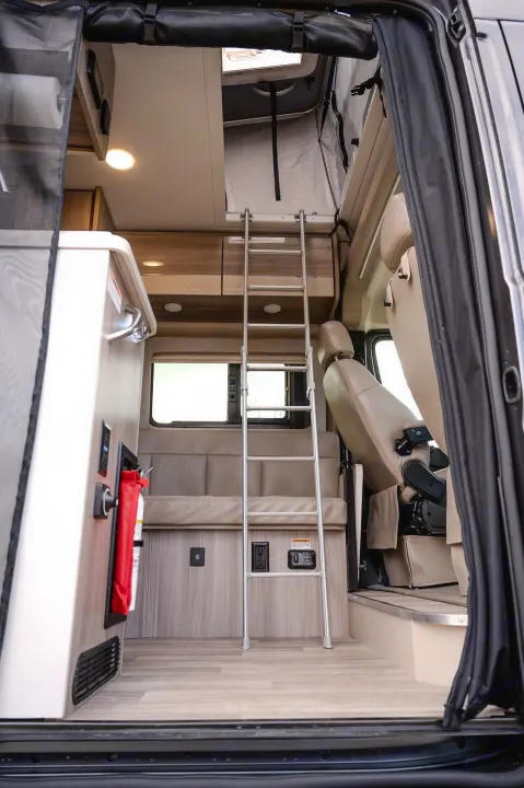 An RV rental's bright interior: a ladder ascends to a loft bed, with a kitchen counter and seating visible below.. Thor Sequence 2024