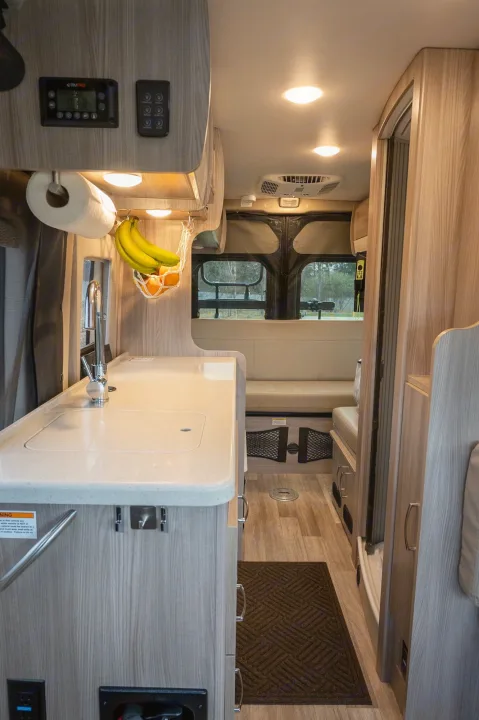 RV rental interior: Light wood kitchen counter, sink, overhead controls, and cozy seating in a compact camper.. Thor Sequence 2024