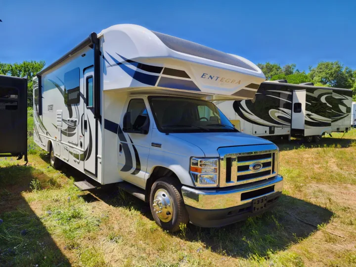 White Entegra Odyssey Class C RV rental, on a Ford E450 chassis, parked on a sunny grass lot with other RVs nearby.. Entegra Coach Odyssey 2021