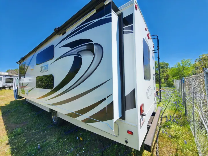 White Entegra Odyssey RV rental with a slide-out extended, parked on green grass under a clear blue sky. Ready for travel!. Entegra Coach Odyssey 2021