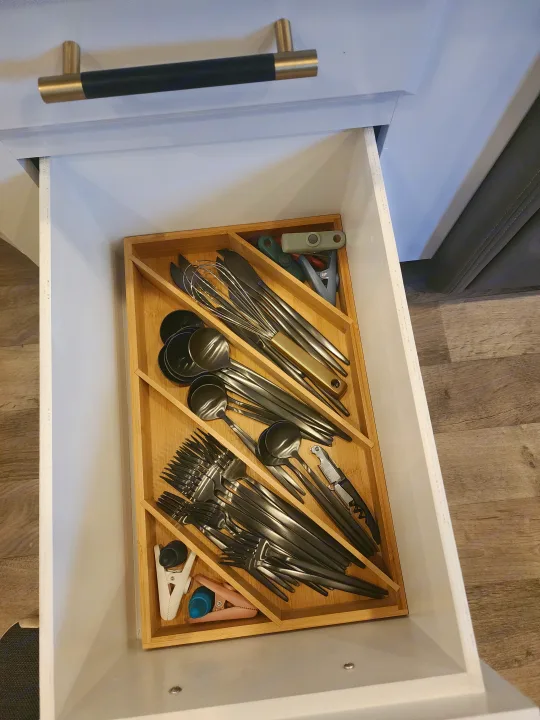 RV rental kitchen drawer open, revealing a bamboo utensil organizer with dark silverware, cooking tools, and clips.. Entegra Coach Odyssey 2021