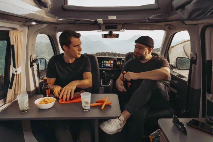 Inside a modern **rv rental**, two friends share snacks & drinks with stunning mountain views, perfect for road trips.. Volkswagen Transporter T6.1 2022