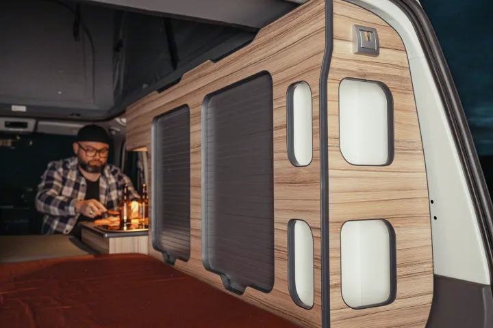 Inside an RV rental: a man cooks in a compact campervan kitchen with sleek wooden cabinetry and storage for adventure.. Volkswagen Transporter T6.1 2022