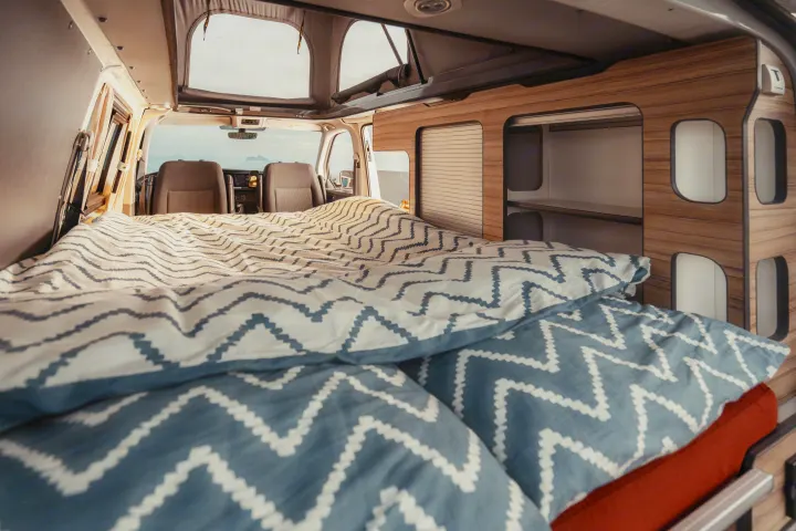 Cozy RV rental interior with bed, built-in cabinets, and a scenic view from the front seats. Perfect for a road trip adventure.. Volkswagen Transporter T6.1 2022