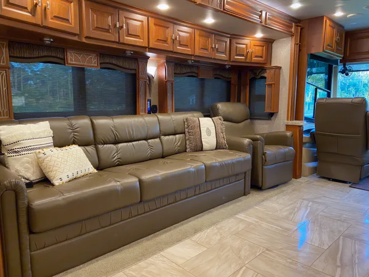 Spacious RV rental living room featuring a long leather sofa, comfortable recliners, and warm wood cabinets above windows.. Tiffin Motorhomes Allegro Bus 2017