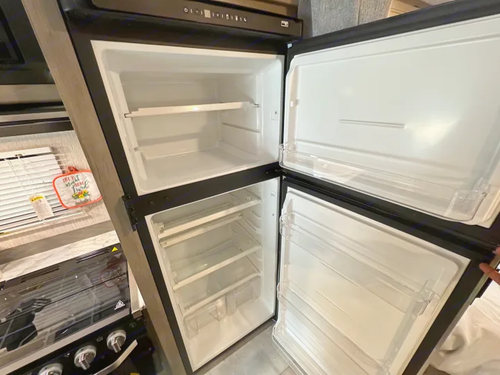Inside an RV rental: empty, open two-door refrigerator & freezer with shelves, ready for groceries in the kitchen.. Coachmen Other 2022