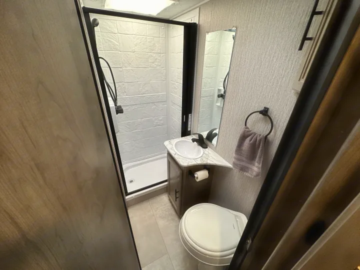 Inside an **rv rental** bathroom with a compact shower, vanity sink, toilet, and mirror. Modern and efficient for travel.. Coachmen Other 2022