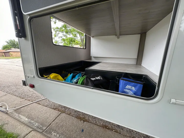 Open RV rental pass-through storage compartment, revealing camping gear including a leveling kit, hoses, and bags for easy access.. Coachmen Other 2022