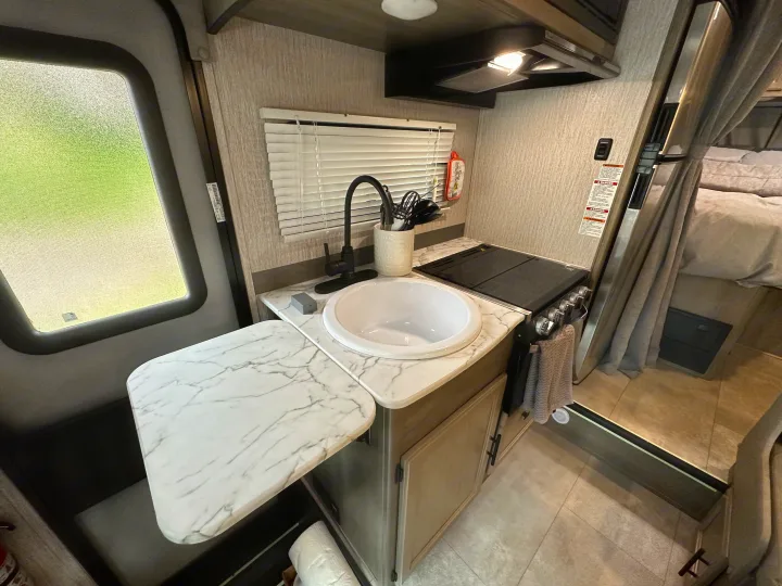 RV rental interior: A compact kitchen with a white sink, black stovetop, extendable counter, and adjacent sleeping area.. Coachmen Other 2022