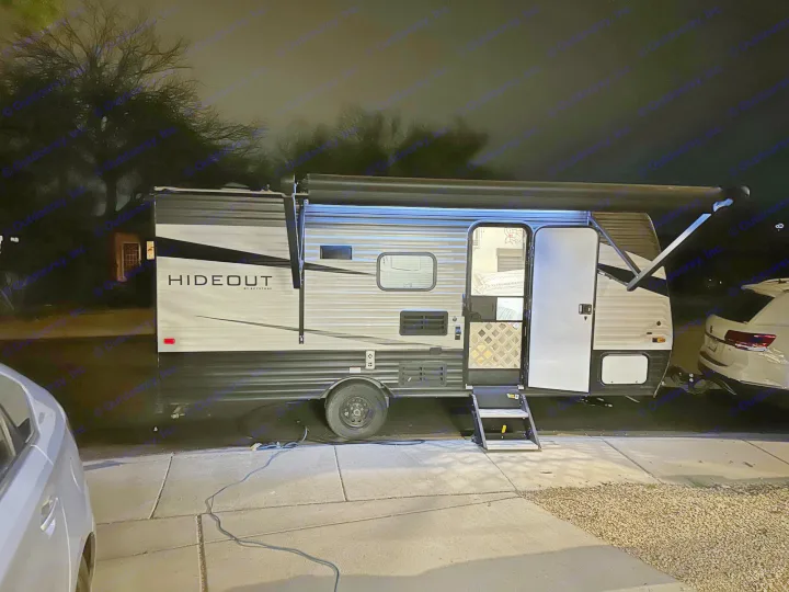 Night setup of an RV rental: a modern travel trailer lit up under its awning, parked in a driveway.. Keystone RV Hideout 2021