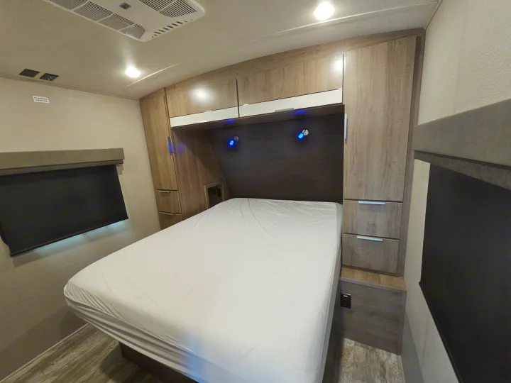 Well-equipped RV rental bedroom featuring a bed with white sheets, ample storage cabinets, and blue reading lights.. Grand Design Imagine 2021