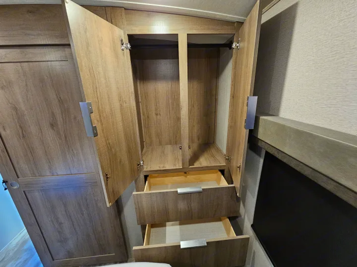 Open RV rental wardrobe with hanging rod and two pulled-out drawers, displaying practical interior storage solutions.. Grand Design Imagine 2021