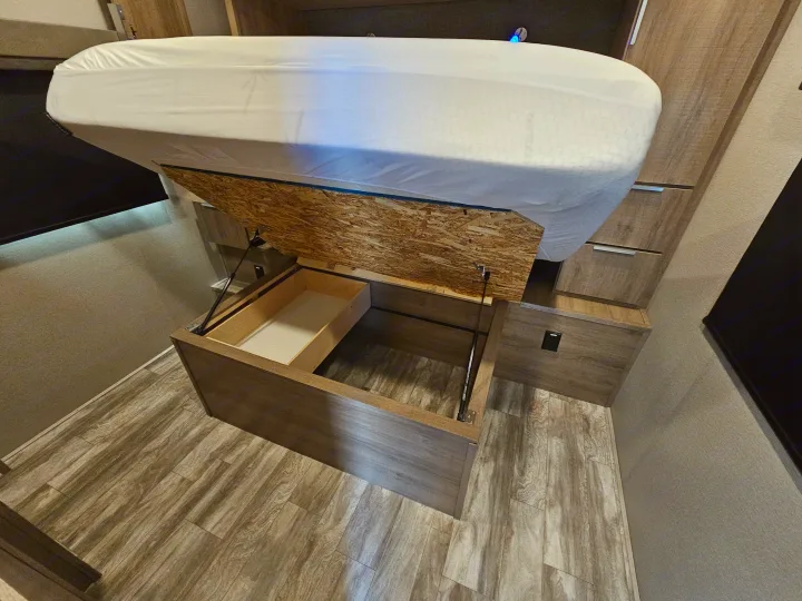 This RV rental bed lifts to unveil spacious under-bed storage with a handy pull-out drawer, optimizing space for travel.. Grand Design Imagine 2021