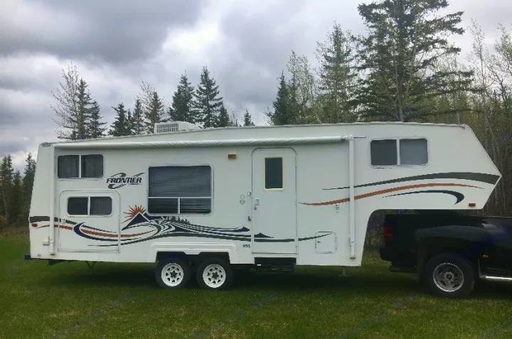 White fifth-wheel RV rental hitched to a black truck on green grass, with evergreen trees under an overcast sky. Perfect for camping.. Frontier FW255 2012