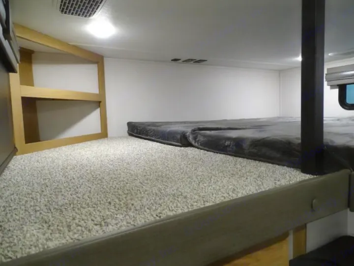 View inside an RV rental: a carpeted sleeping area with two grey mattresses on the floor and light wood shelves.. Primetime Sanibel 3602WB 2023