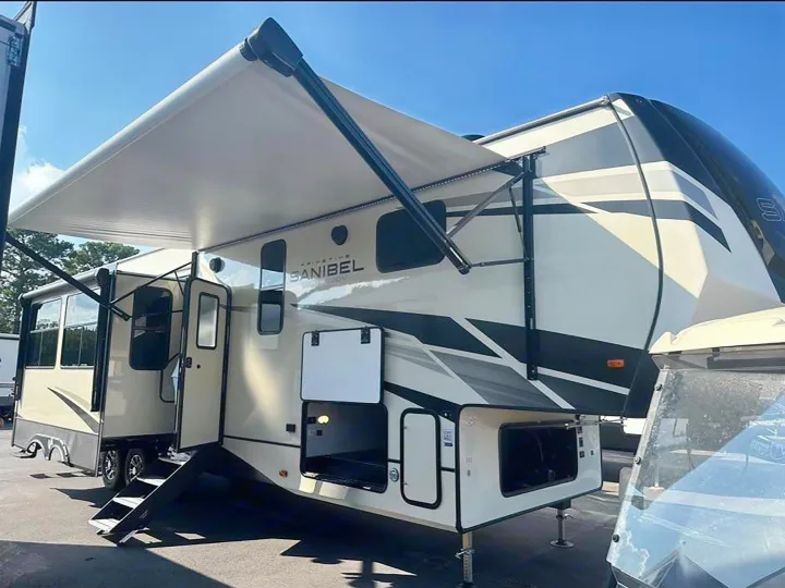 Spacious RV rental: a beige fifth-wheel trailer with an awning extended, showing open storage and entry steps.. Primetime Sanibel 3602WB 2023
