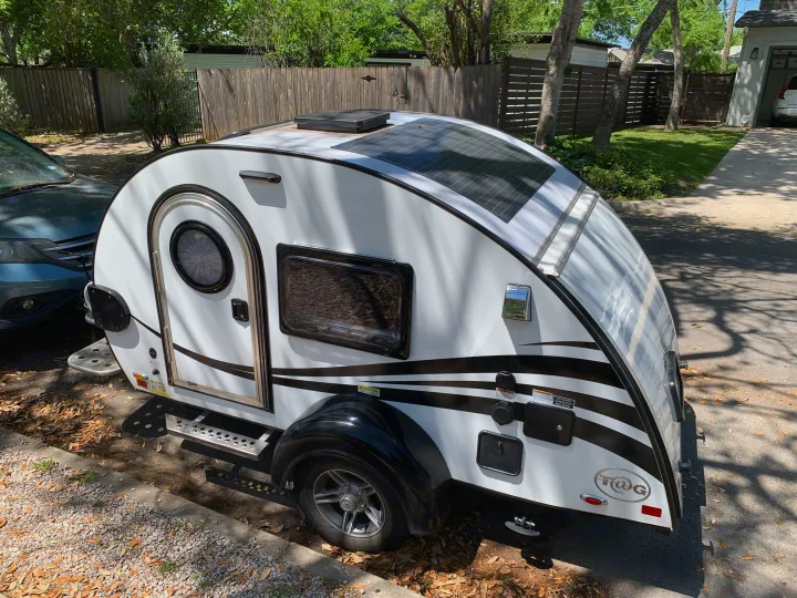 White T@G teardrop trailer with black stripes and solar panels, perfect for an RV rental adventure, parked outside.. nuCamp T@G 2022