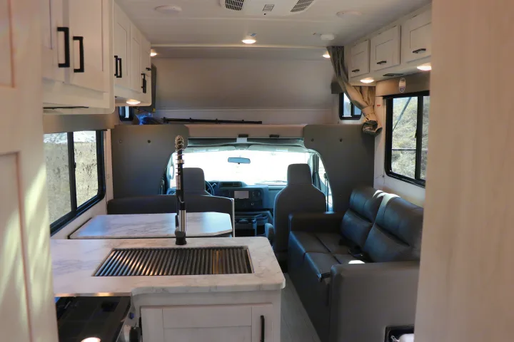 Interior of a modern rv rental showing the kitchen area, dinette, lounge seating, and cab-over bunk for a comfortable journey.. East to West entrada 2025