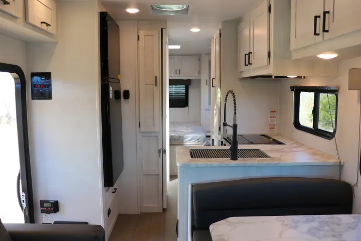 Spacious RV rental interior: modern kitchen with sink, refrigerator, and control panel, leading to a visible bedroom.. East to West entrada 2025