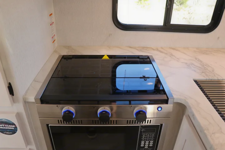 This RV rental kitchenette features a sleek stove with a glass cover, illuminated knobs, and a built-in oven.. East to West entrada 2025