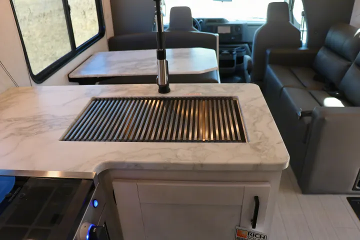 This RV rental offers a modern kitchen with a marble-look counter, integrated sink/drying rack, stove, and dining area.. East to West entrada 2025