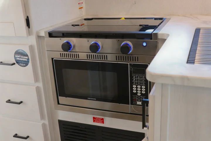 This RV rental kitchen features a Greystone microwave/oven combo, stovetop with blue LED knobs, and soft-close drawers.. East to West entrada 2025