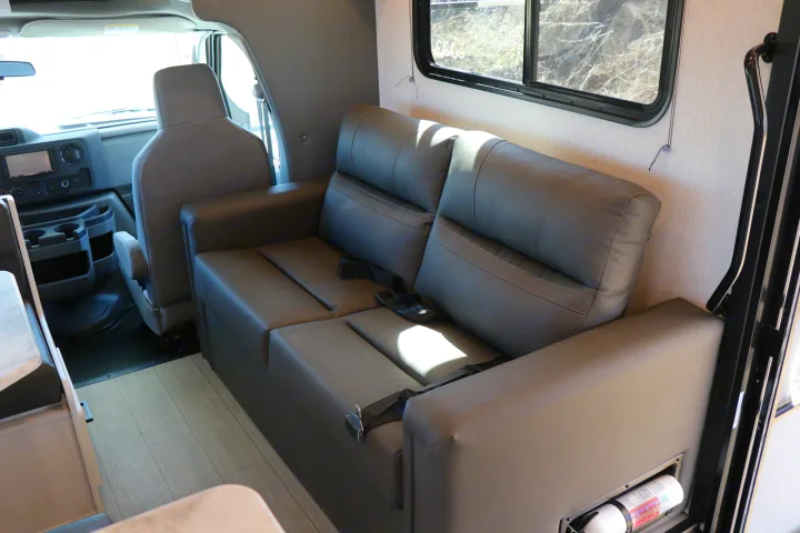 Inside an rv rental, featuring the driver's area and a gray sofa with seatbelts, showing a spacious interior layout.. East to West entrada 2025