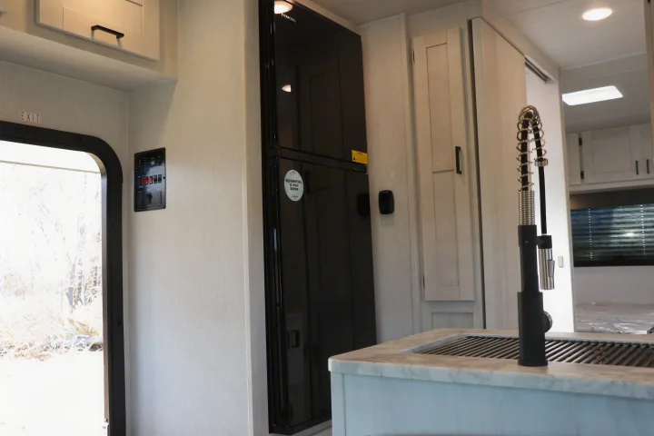 Modern RV rental interior with a black refrigerator, detailed control panel, and sleek kitchen sink setup.. East to West entrada 2025