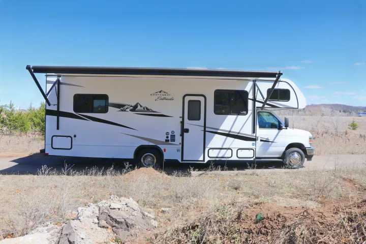 A white East West Entrada RV rental with an extended awning is parked outdoors under a clear blue sky, ready for adventure.. East to West Entrada 2025