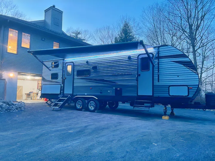 This RV rental is parked at dusk beside a home, with its bright awning lights on.. Forest River Aurora 28BHS 2024