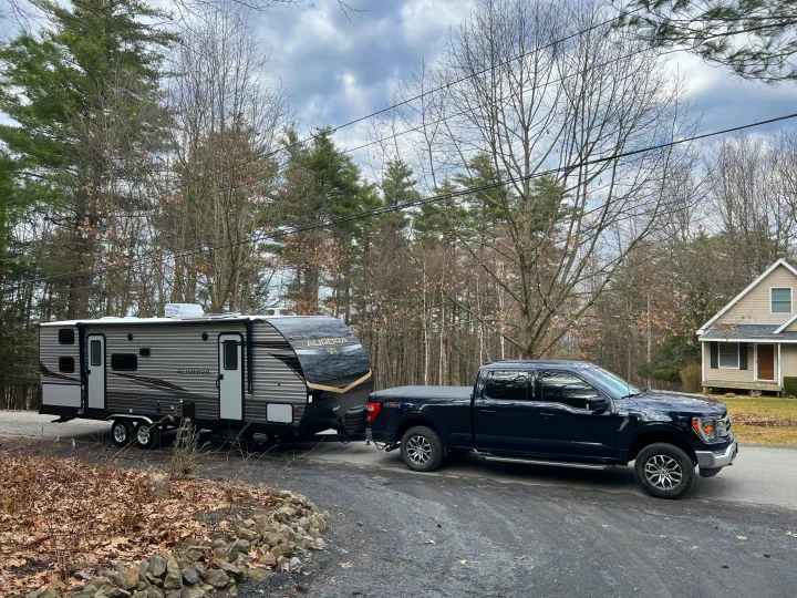 Black Ford F-150 truck hitched to a grey 'Aurora' travel trailer RV on a paved driveway. Ideal for RV rental trips.. Forest River Aurora 28BHS 2024