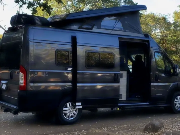 Dark gray Winnebago Solis rv rental with extended pop-top and open side door, parked outdoors.. Winnebago Solis 2023