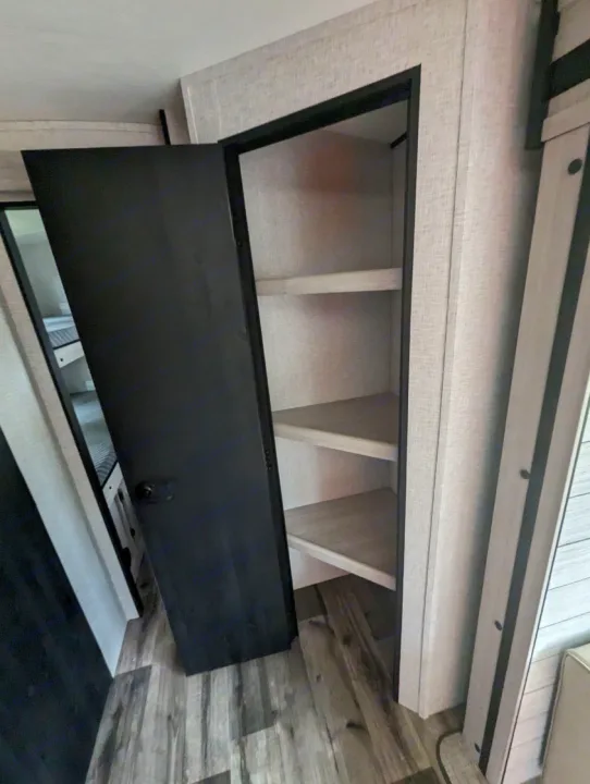 RV rental bunkhouse area: A black door opens to compact storage shelves, with bunk beds seen inside.. Crossroads RV Sunset Trail Superlite 2024