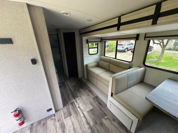 Inside a modern RV rental, showing the comfortable living area with sofa, dinette, wood flooring, and windows looking outside.. Crossroads RV Sunset Trail Superlite 2024