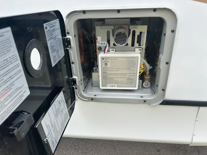 Open access panel on an RV rental revealing a Girard tankless water heater with visible operating instructions and safety warnings.. Crossroads RV Sunset Trail Superlite 2024